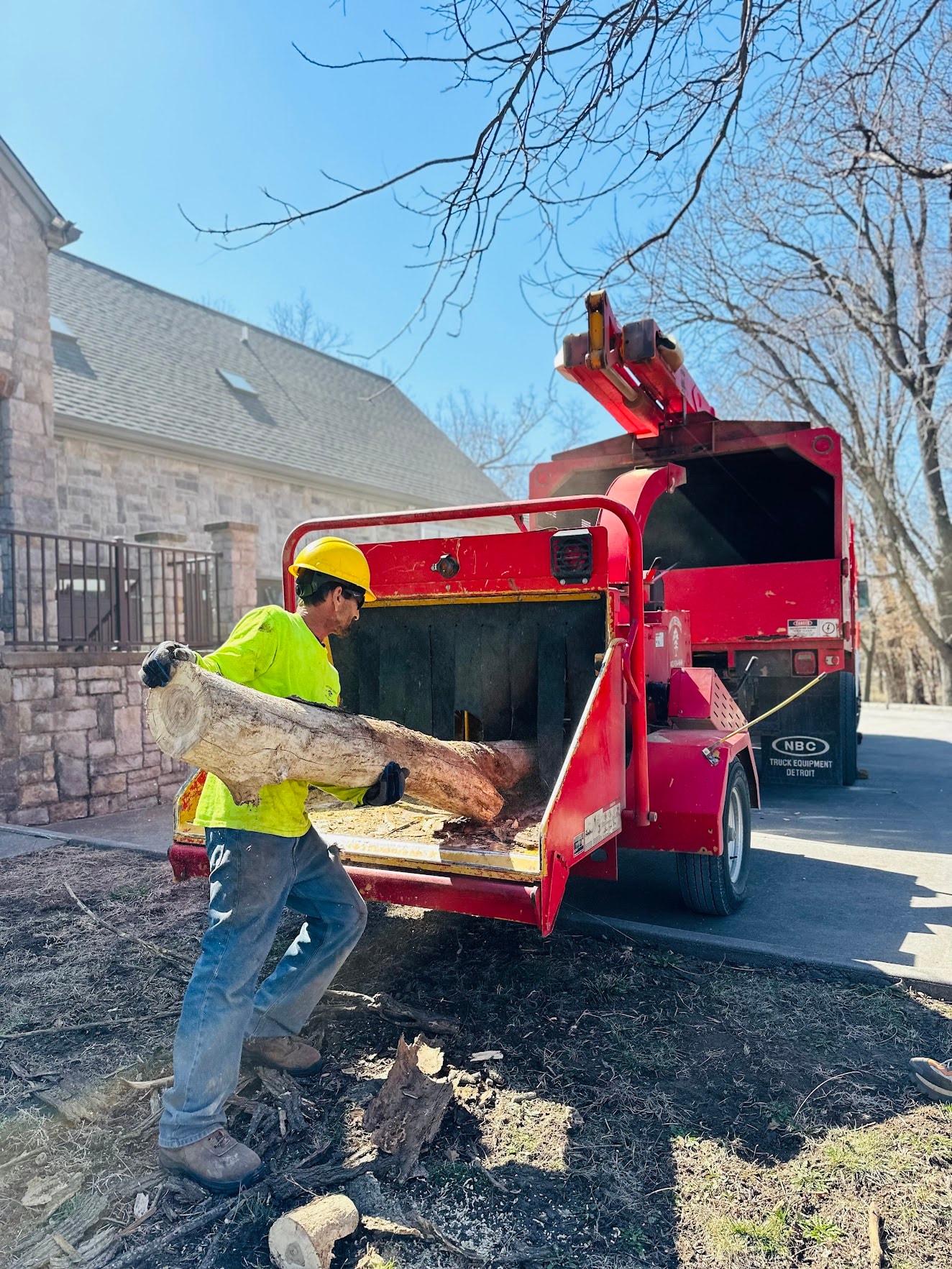 Vinny's Tree Service crew member loading logs into chipper truck at residential job site